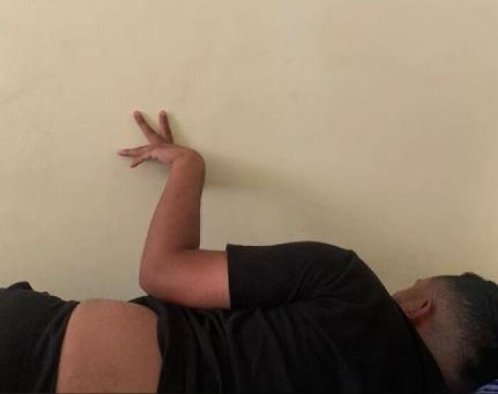 Person caught sleeping in hilarious and unhinged pose lying on their side with arm bent awkwardly against the wall.