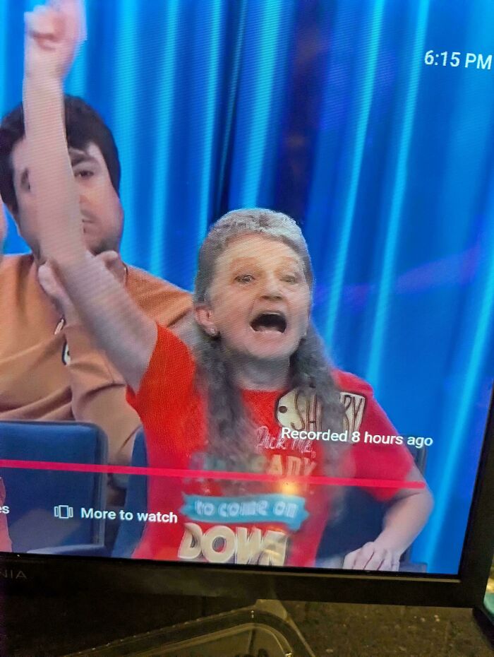 A woman with long, frizzy grey hair and a wild expression, celebrating on a game show, a bad hair mistake.