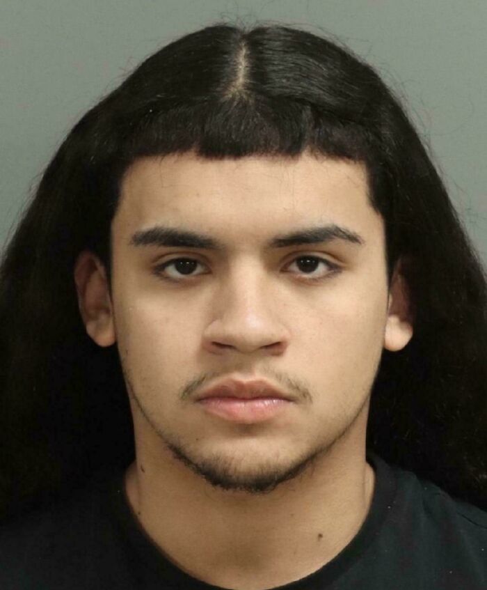 A young man with very long dark hair parted down the middle and extremely short, straight bangs, a bad hair mistake.