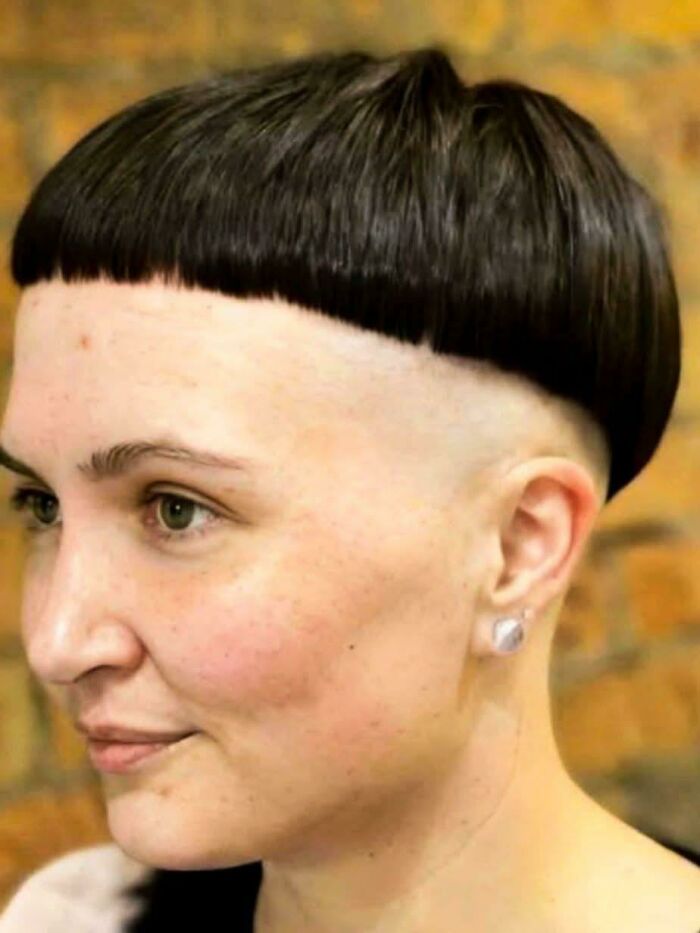 A woman with a bowl cut and shaved sides, a hilariously bad hair mistake, smiles slightly.