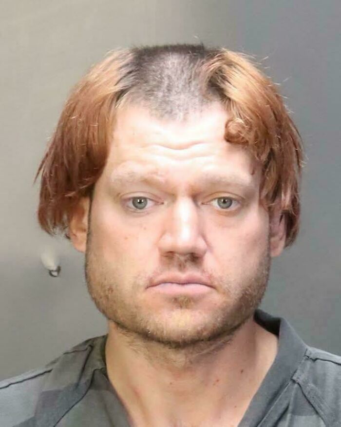 Mugshot of a man with a bad hair mistake, including a partially shaved head and long bangs.