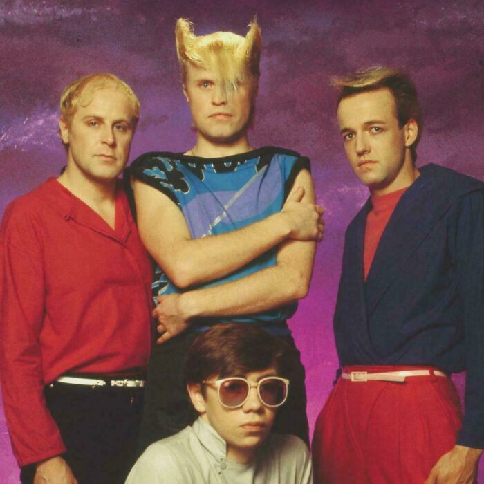 Four individuals in retro attire with exaggerated and bad hair mistakes from the 80s.