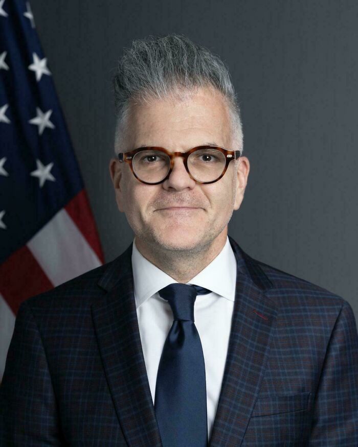 A man in a suit with a modern undercut and gray hair, a subtle hair mistake.
