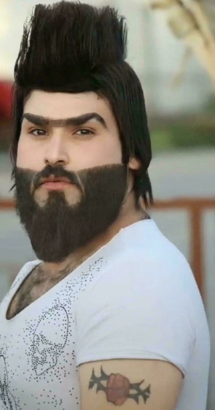 Man with a tall mohawk, thick beard, and unibrow, showcasing hilariously bad hair choices.