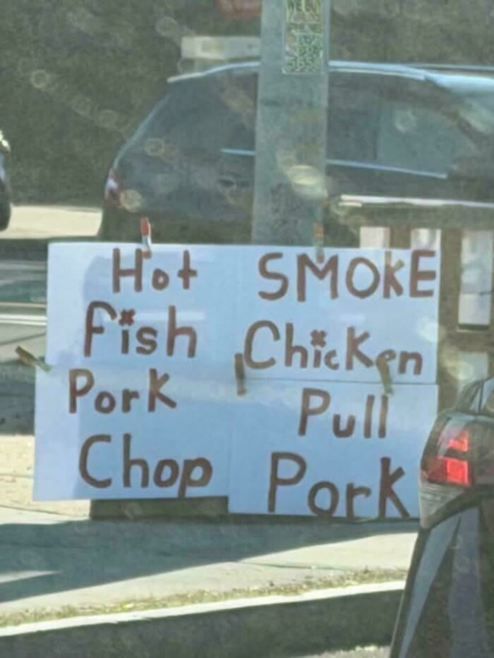 A handwritten sign by a road with a confusing message for food items like 'Hot Fish Pork Chop' and 'SMOKE Chicken Pull Pork'.