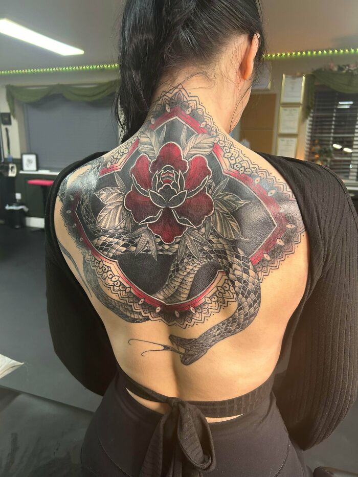 A person shows off a stunning full back tattoo featuring a red rose and a snake in an ornate frame, a happy, forever body art choice.