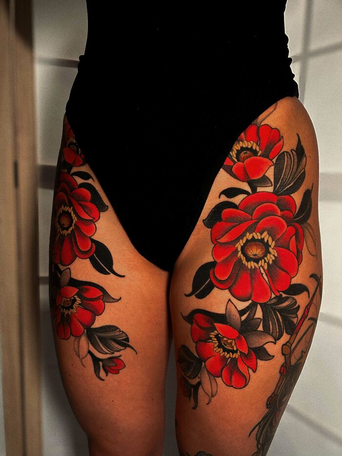 A person displays stunning tattoos of red flowers with black leaves on both thighs, symbolizing happiness and permanent body art.