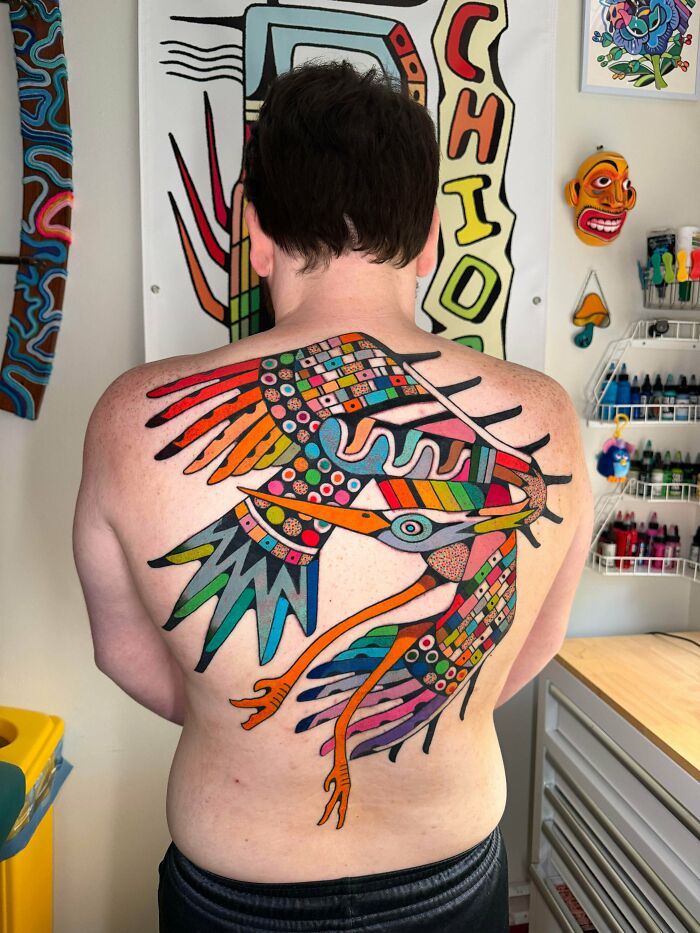 A person's back completely covered with a large, colorful, abstract bird tattoo, a stunning example of tattoos.