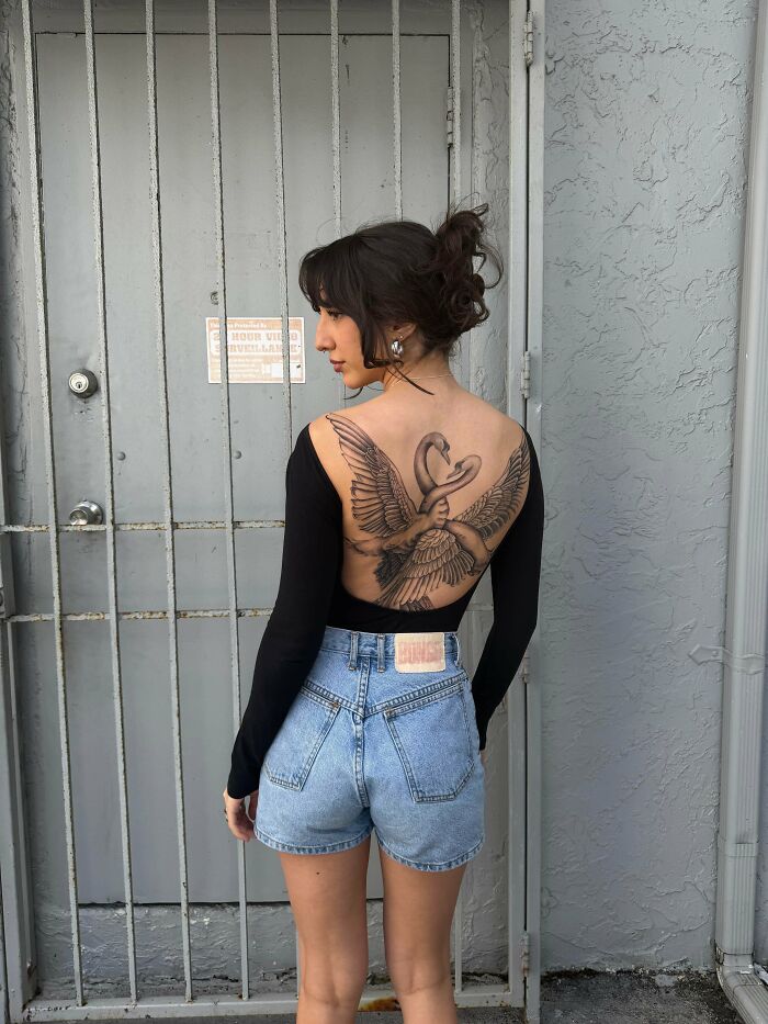 A woman with an elaborate back tattoo of two swans with interlocking wings, showcasing beautiful tattoos.