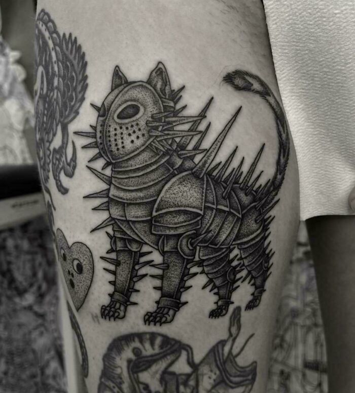 A black and white tattoo of a spiky cat in armor on a person's leg, one of many stunning tattoos.