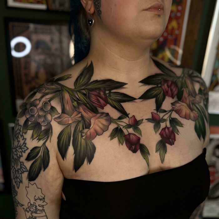 A vibrant floral chest and shoulder tattoo, featuring purple and green flowers, displaying stunning tattoos.