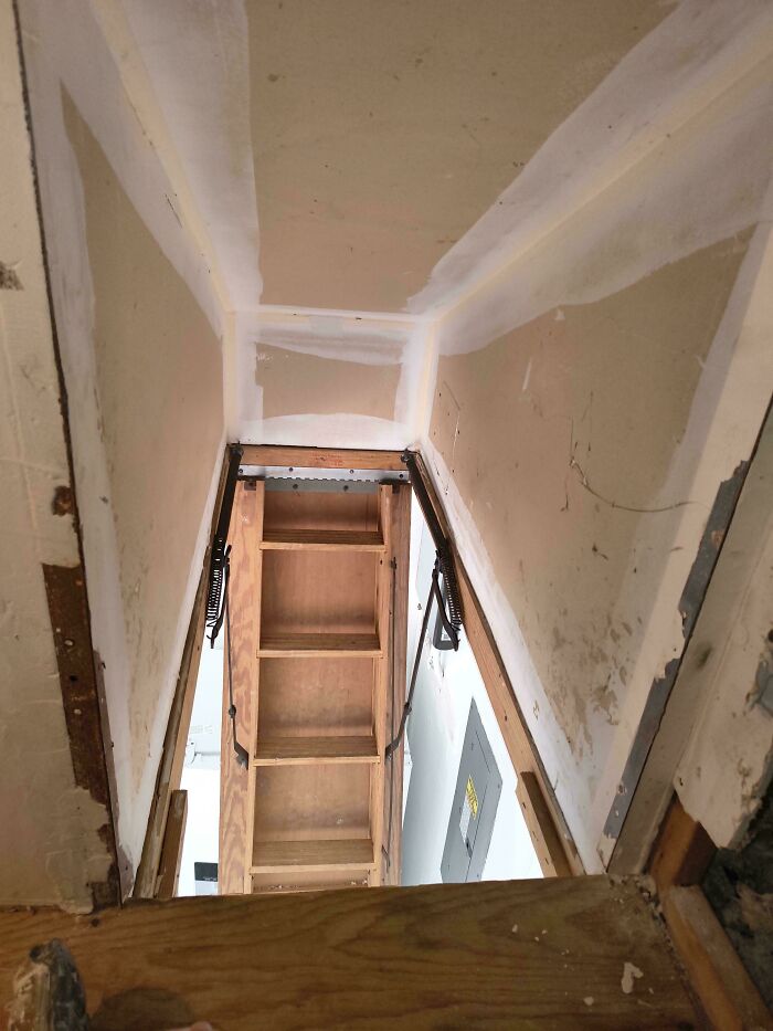 A questionable DIY project showing an unsafe attic ladder setup through a drywall opening.