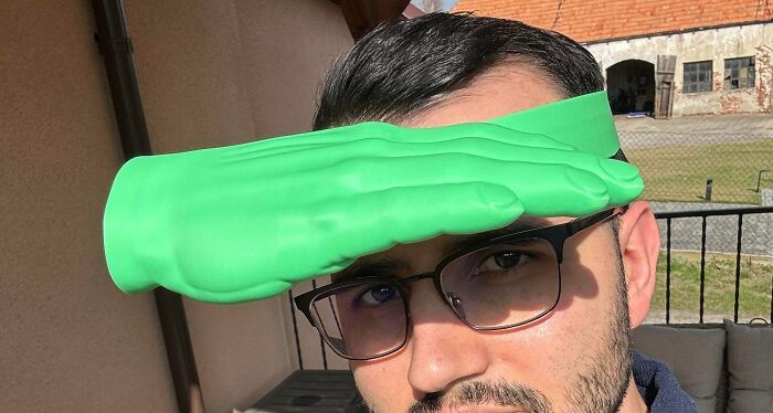 Man wearing a green rubber hand attached to his forehead as a sun visor in a questionable DIY project.