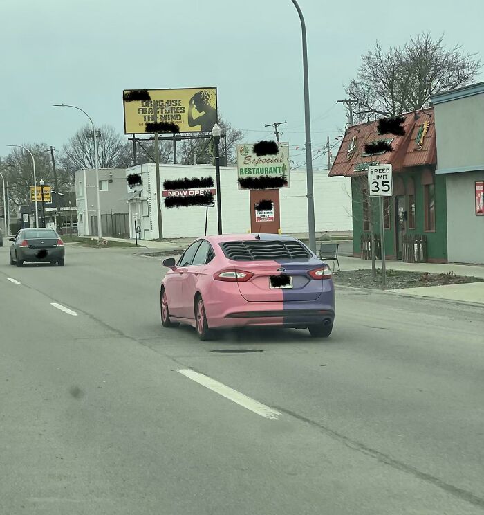 Split painted pink and purple sedan driving down a street, showcasing questionable DIY projects.
