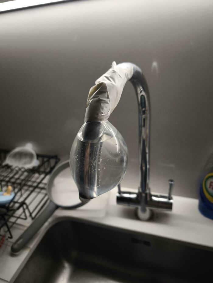 Kitchen faucet taped with a water-filled plastic bag in a funny DIY repair.