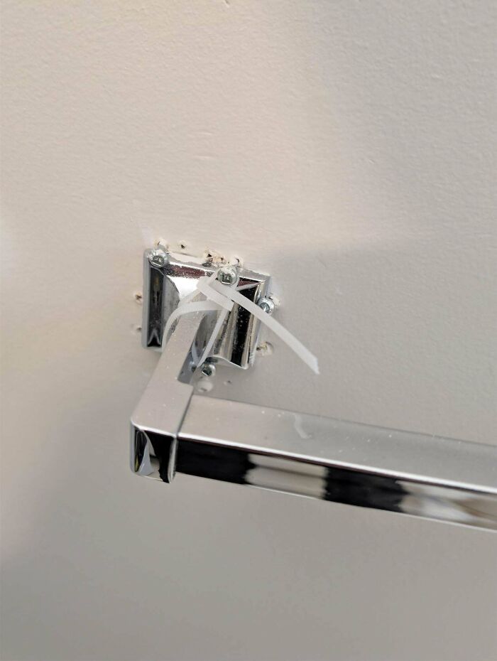 A chrome bathroom towel rack fixed to a wall using plastic zip ties, showcasing questionable DIY projects.