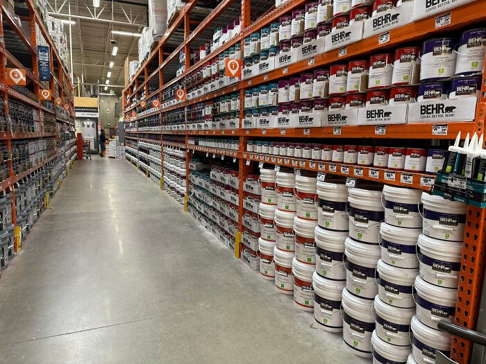 A long, organized aisle of paint cans on shelves inside a retail store representing Home Depot employees posts