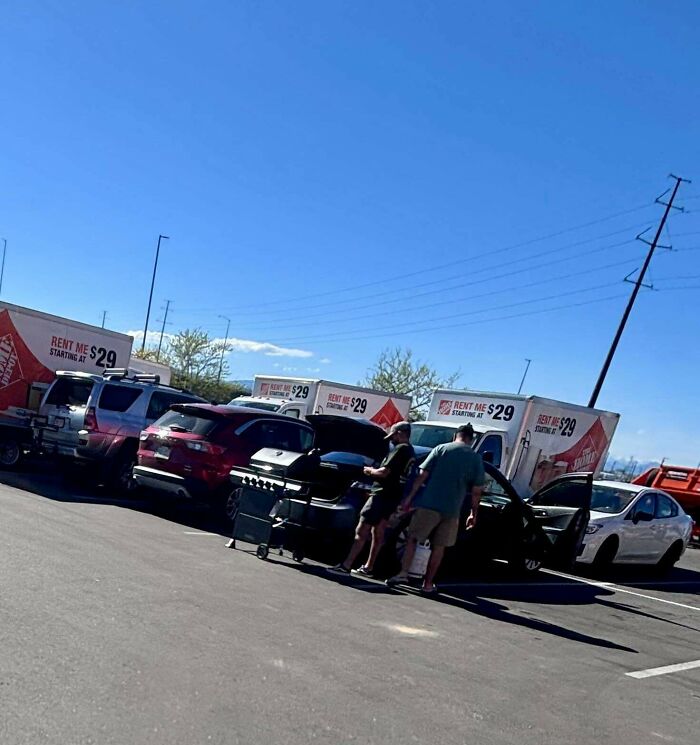 Customers loading a barbecue grill into a sedan next to orange Home Depot rental trucks