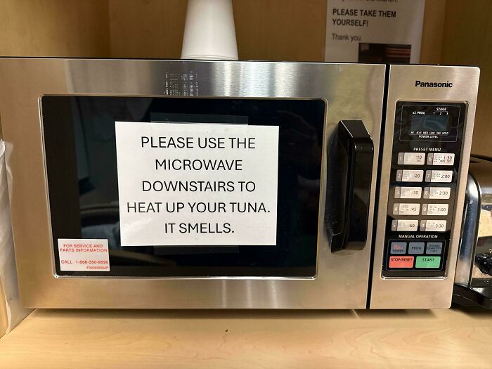 A microwave with a passive-aggressive note asking users to heat tuna downstairs because it smells.