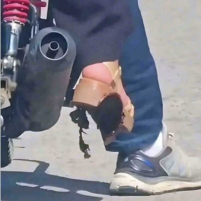 A person with a peculiar thing: a high heel stuck to their pants, next to a motorcycle exhaust.