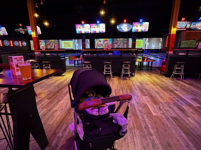 A baby stroller in a lively bowling alley, showing an online community of dads relaxing.