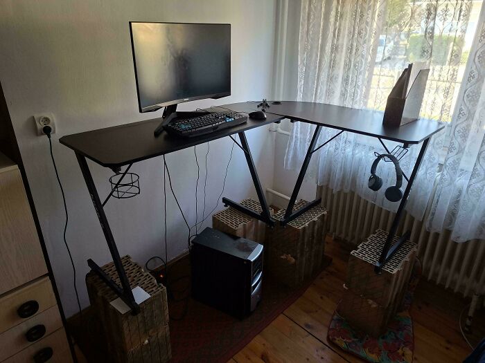 A L-shaped desk with a monitor, keyboard, and headphones, creatively raised with wicker baskets—a frugal tip for this economy.