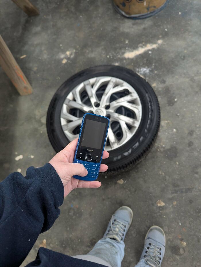 A person holds a blue Nokia phone over a car tire on a concrete floor, representing frugal tips in this economy.