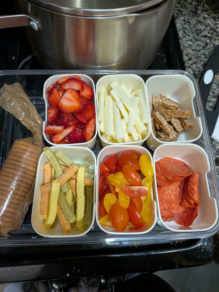 A bento box filled with strawberries, cheese sticks, crackers, veggie sticks, cherry tomatoes, and pepperoni, showing frugal tips for snacks.