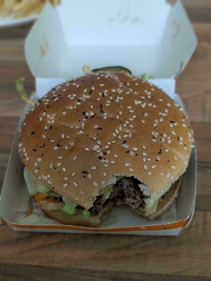 A partially eaten hamburger with a bite taken out of it, sitting in its paper box, from the Not Interesting community.