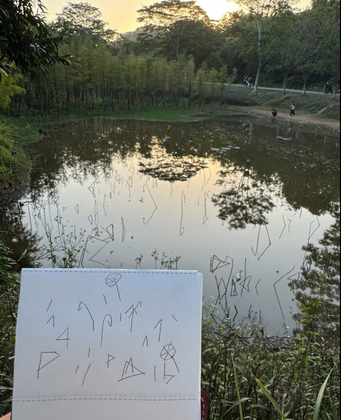 A drawing on a notepad held up against a serene lake backdrop, from the Not Interesting Community.