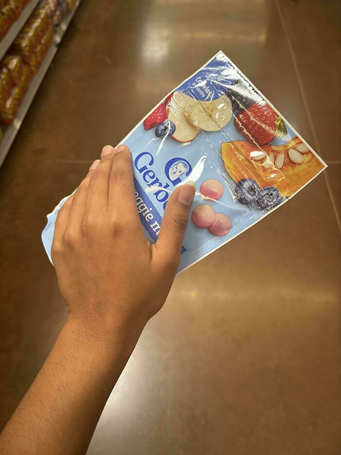 A hand holding a Gerber baby food pouch with fruit illustrations, a photo from the Not Interesting Community.