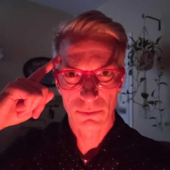 A man with red glasses and a red glow pointing to his temple, part of the Not Interesting Community.