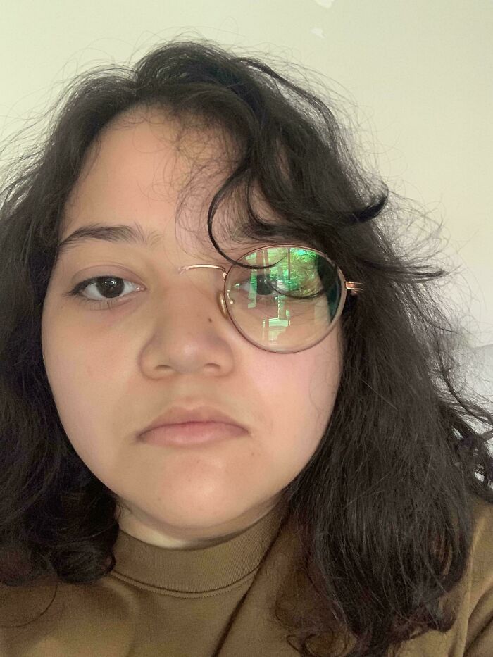 A person with long dark hair and one circular spectacle lens covering their right eye, a photo from the Not Interesting community.