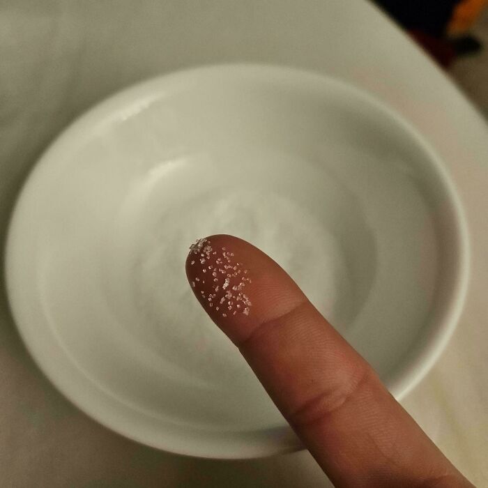 A finger with a few grains of sugar on it, over a white bowl, a picture from the Not Interesting community.