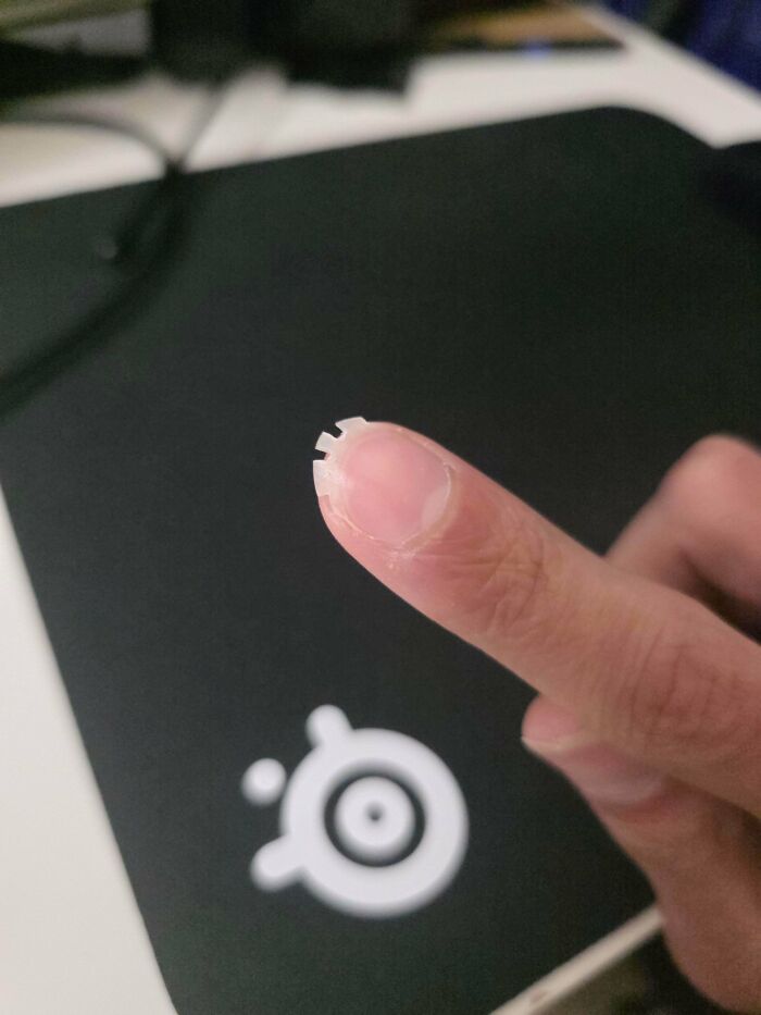 A person's finger holding a tiny, intricate plastic piece over a mousepad, from the not interesting community.