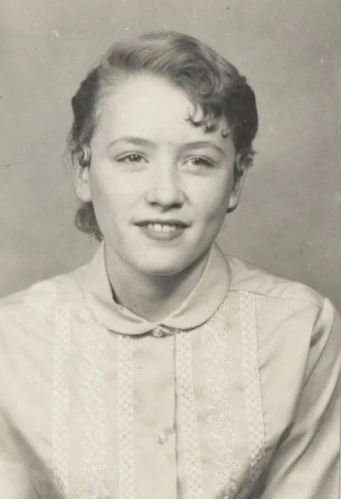 A black and white historical photo of a smiling young woman with curly hair, wearing a collared shirt.