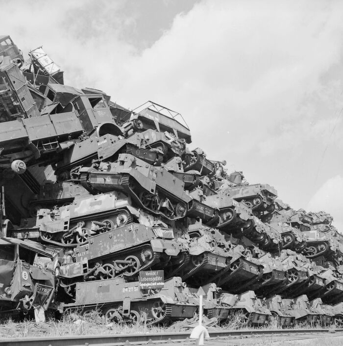 A striking historical photo depicting a massive pile of destroyed military vehicles and tanks under a cloudy sky.