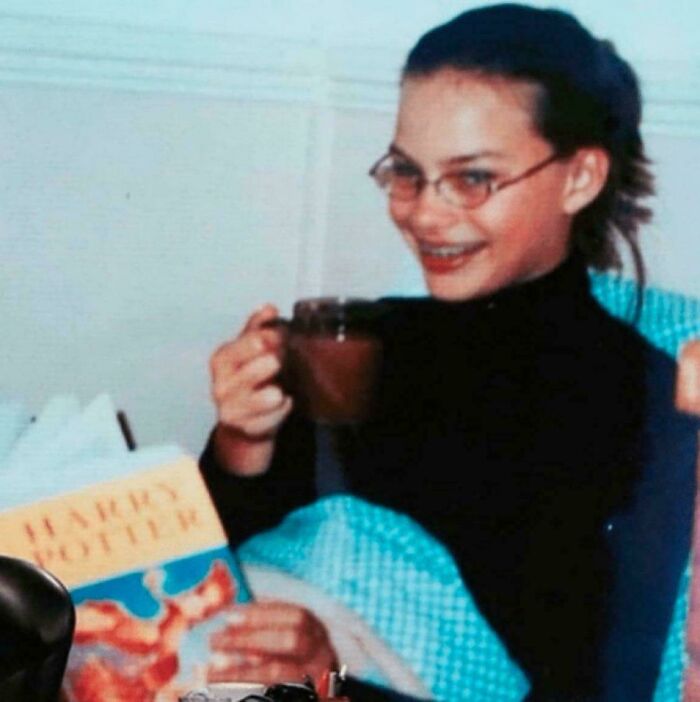 A historical photo of a young girl with glasses and braces, holding a mug and a Harry Potter book.