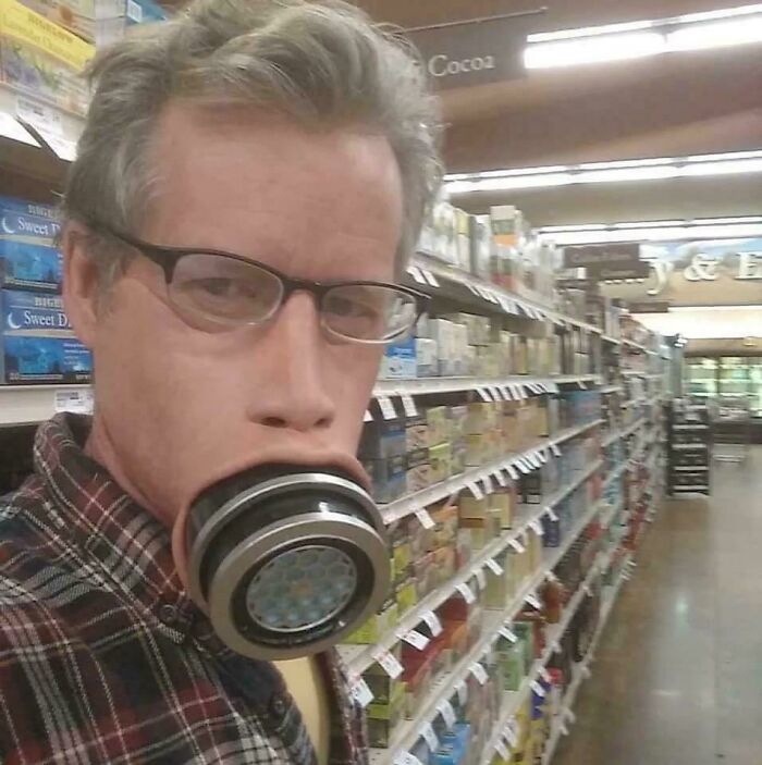 Person in glasses wearing a bizarre face mask resembling a mechanical device in grocery store aisle