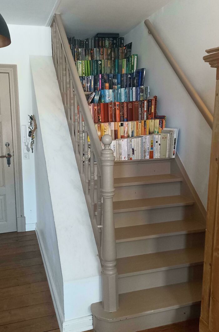 A staircase with an impressive collection of books arranged by color on the steps, a mildly interesting picture.