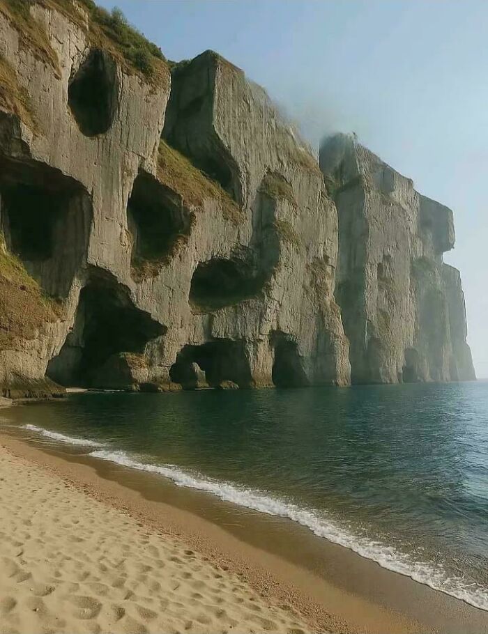A stunning view of sea cliffs with multiple cave openings and a sandy beach, hinting at fascinating geological formations or online lies.