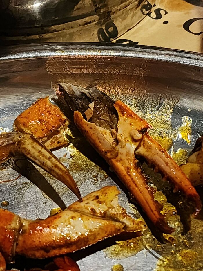 A baffling image of a metal plate with leftover crab claws and shells, covered in sauce and remnants.