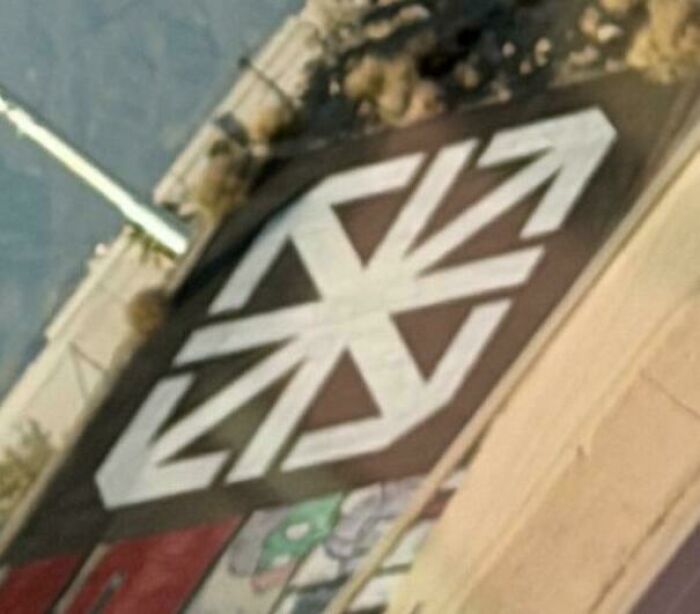 A baffling image of a large, distinctive white arrow symbol painted on a dark surface from an aerial view.
