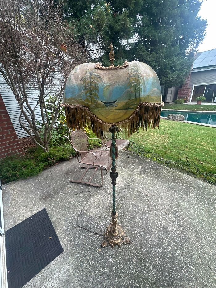A remarkable antique floor lamp with a painted scenic shade and fringe, standing outdoors by a pool.