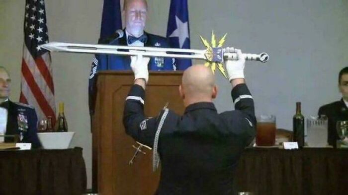 A man holds a large, peculiar sword over his head during a formal event. People spotted this unusual scene in real life.