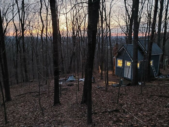 Small home in wooded area with lit windows at dusk showing cozy living