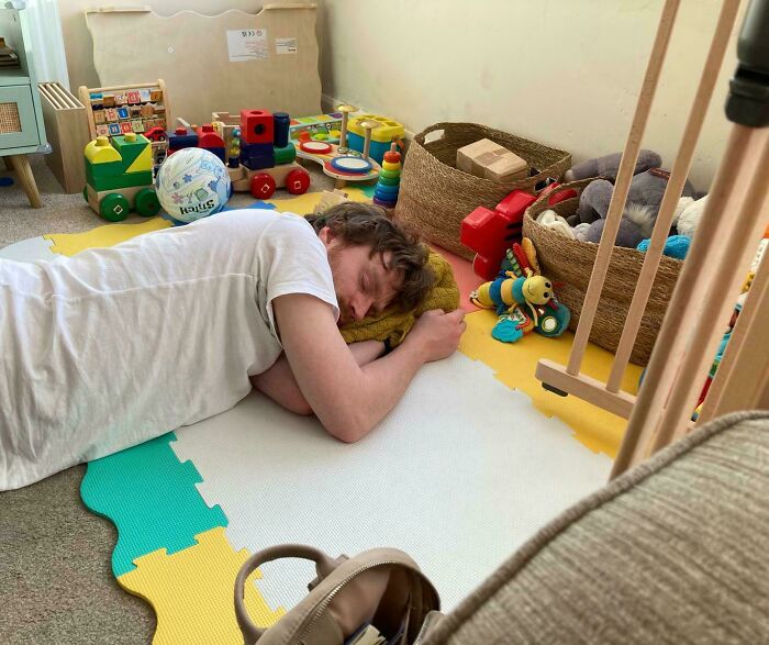 A tired dad sleeps on a playmat surrounded by kids toys, highlighting the dedication of fathers.