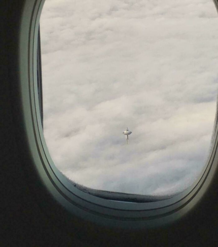 A unique perspective of the Seattle Space Needle peeking through thick clouds from an airplane window, a truly interesting photo.
