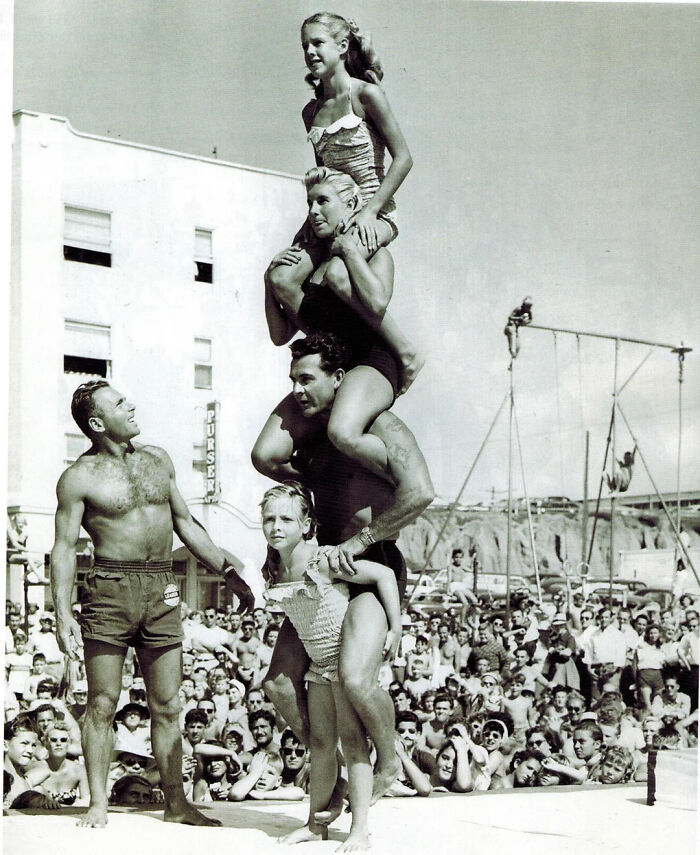 An interesting vintage photo shows four acrobats forming a human pyramid on a beach, with a crowd watching.