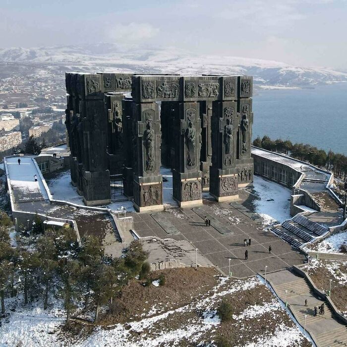 An interesting photo of a massive, intricately carved stone monument against a snowy mountain and lake backdrop.